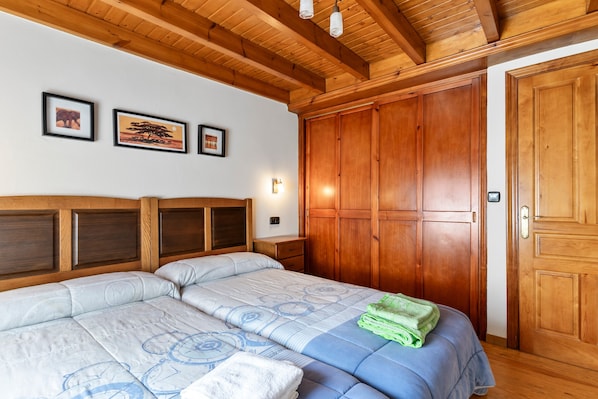 Ein Schlafzimmer mit zwei Betten, Holz-Kopfteilen, einem Kleiderschrank und gerahmten Bildern an der Wand.