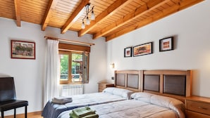 A bedroom with a wooden ceiling, a bed with a headboard, a chair, a window with curtains, and framed pictures on the wall.