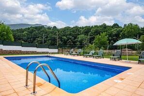 A swimming pool with a tiled deck, lounge chairs, and an umbrella.