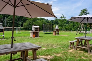 A grassy outdoor area with picnic tables and barbecue grills.