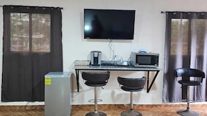 A room with a tiled floor, a flat-screen TV mounted on the wall, a small refrigerator, a microwave, and two bar stools. - PLEASANT HOSTAL PANAMA (24 de Diciembre)