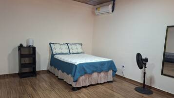 Une chambre avec un lit, un ventilateur sur pied, une étagère et un climatiseur.