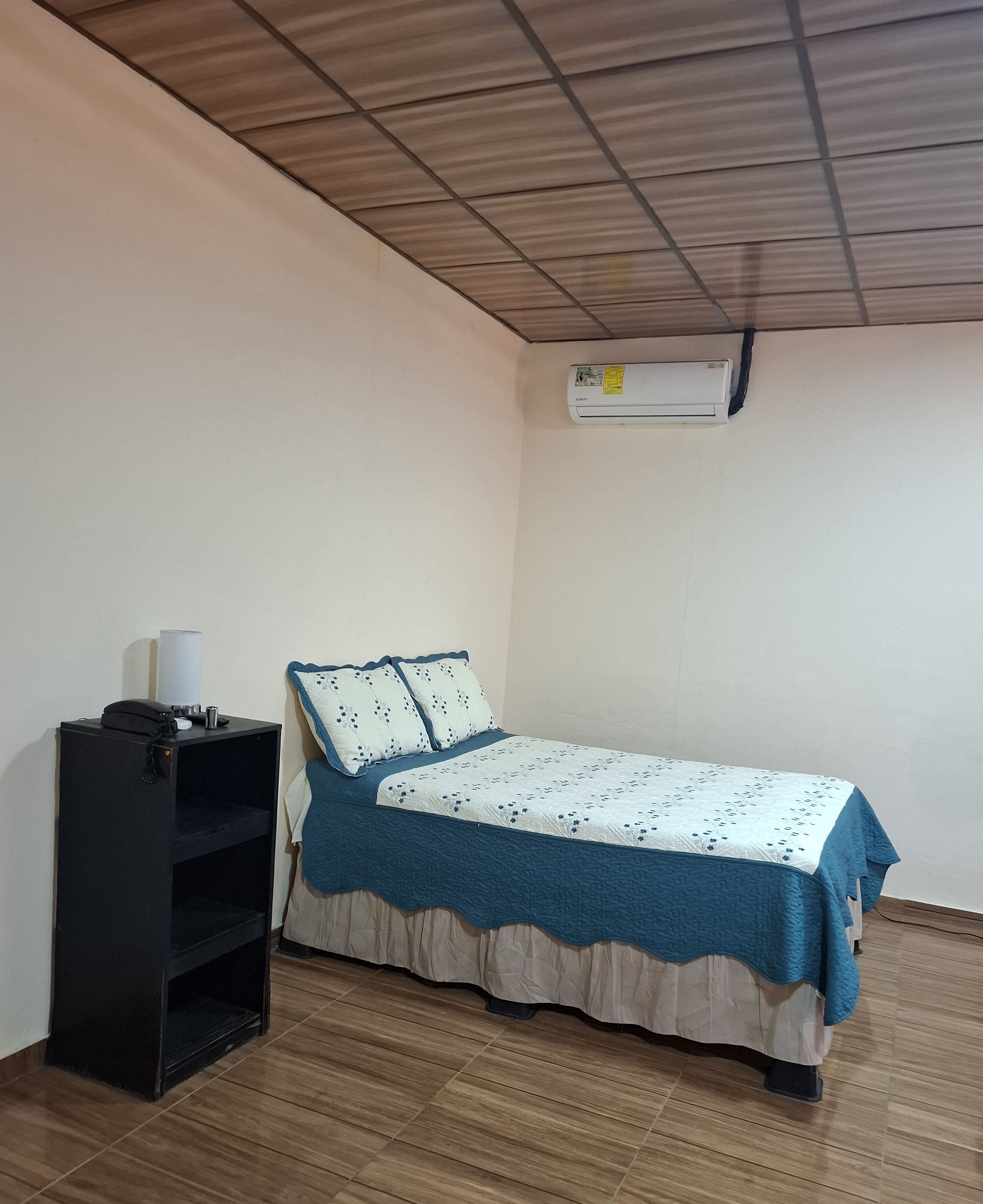 A small, neatly arranged bedroom with a bed, a black shelf, and a ceiling fan.