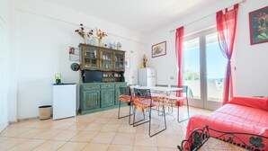 Una habitación con mesa de comedor, sillas, cama, kitchenette y balcón con cortinas rojas.