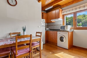A compact kitchen with wooden cabinets, a washing machine, a microwave, and a dining area with a table and chairs. - Casa rural 'El Trasgu' con vistas a la montaña, piscina y barbacoa (Unknown)