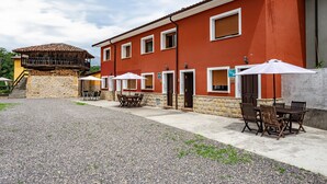 A red building with a stone staircase, outdoor seating with umbrellas, and a view of a mountain. - Casa rural 'El Trasgu' con vistas a la montaña, piscina y barbacoa (Unknown)