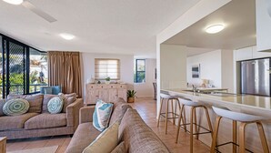 Un salon moderne comprenant un ensemble de canapés, un coin repas avec des tabourets de bar et une cuisine équipée d’un réfrigérateur en acier inoxydable.