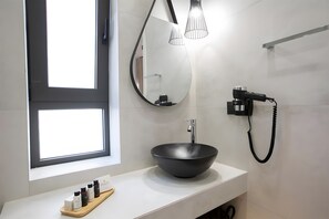 Une salle de bain moderne avec un grand miroir, un lavabo sur colonne noir, un sèche-cheveux et une fenêtre.