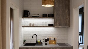 A compact kitchen with white brick walls, a black sink, wooden cabinets, and a hanging light fixture.