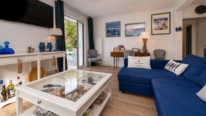 Un soggiorno con un divano blu, un tavolino in vetro, una TV e una vista attraverso una porta vetrata.
