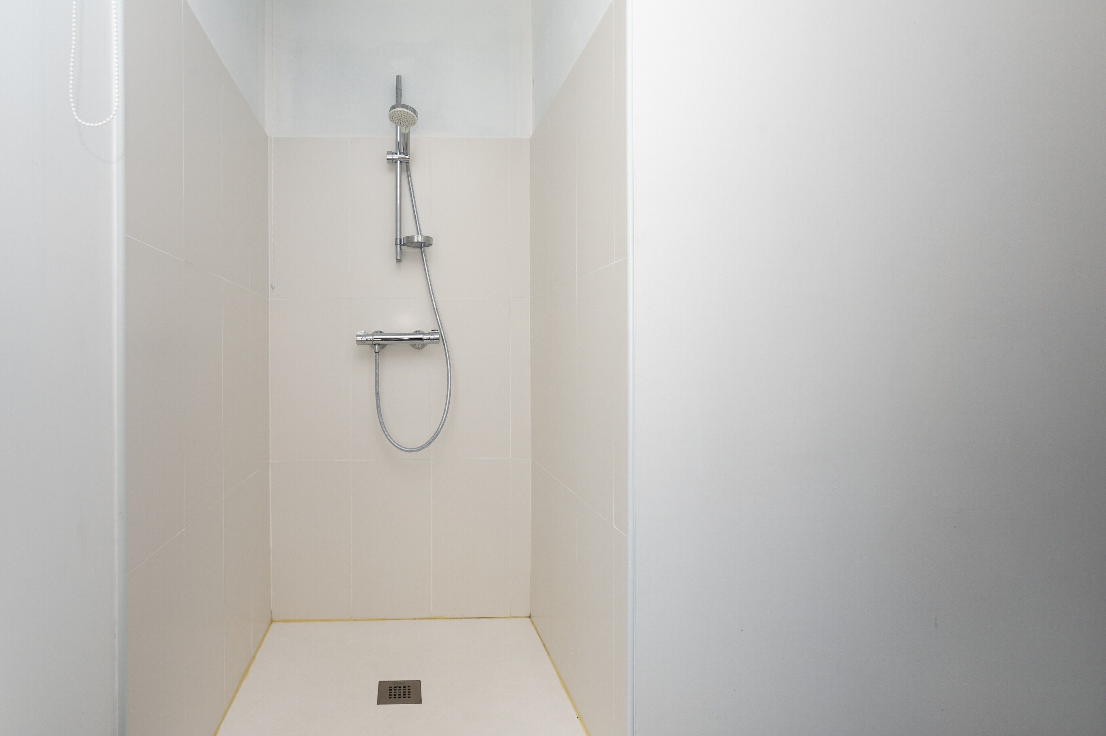 A shower with a handheld showerhead and a wall-mounted faucet in a white-tiled bathroom.
