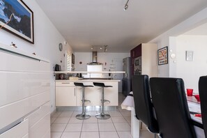 Une cuisine moderne dotée d’un îlot central, de tabourets de bar, d’une table à manger avec des chaises et d’un réfrigérateur.