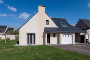 Une maison moderne à deux étages, dotée d’un garage, d’une petite fenêtre au deuxième étage et surplombant un ciel dégagé.