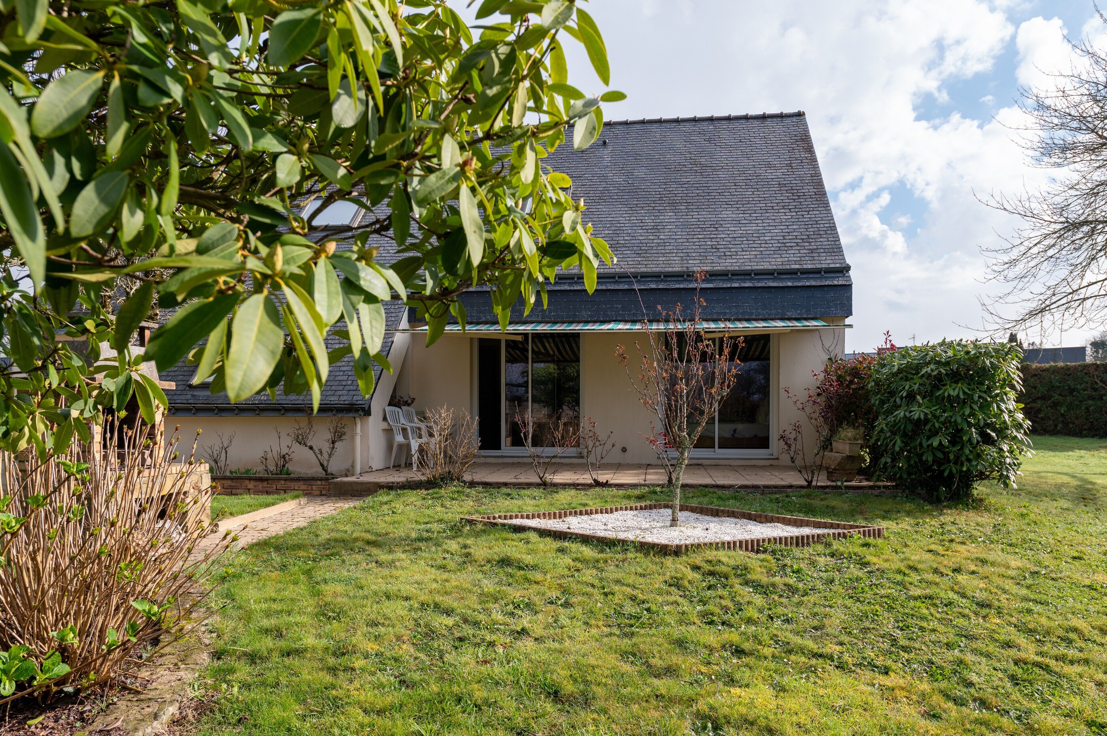 A house with a sloped roof, a front porch, and a small tree in the yard.