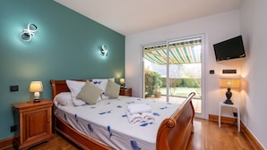A bedroom with a bed, nightstands, a TV, and a view of the outdoors. - Holiday Home 'Entre Terre Et Mer' with Private Terrace, Garden & Wi-Fi (Pluvigner)