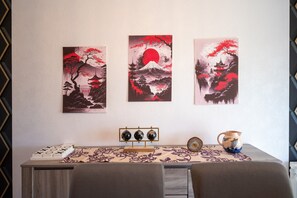 Una pared con tres cuadros, una mesa con un jarrón y un reloj, y un pequeño soporte con tres objetos.