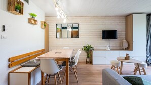 Un espacio habitable moderno con comedor, sofá, televisor y zona de cocina.