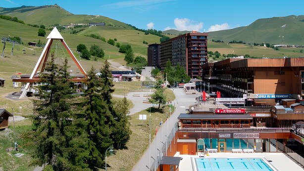 Un hotel con piscina, telesilla y montañas al fondo.