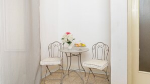 Una habitación pequeña con una cortina a rayas, una mesa redonda con un jarrón de flores, dos sillones acolchados y una ventana.