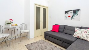 Una sala de estar con un sofá gris, una mesita redonda con sillas, una puerta y una obra de arte colgada en la pared.