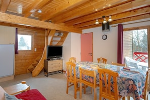 A wooden interior with a dining table, chairs, a TV, and a staircase.