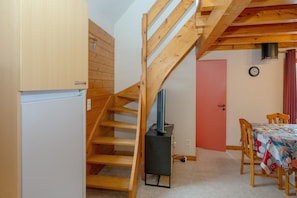 A compact room with a wooden staircase, a small table with a patterned tablecloth, and a clock on the wall.