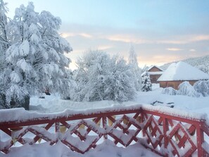 A snow-covered landscape with a red metal fence, trees, and a building in the background.
