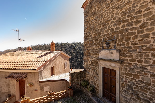 Un edificio de piedra con puerta de madera, una ventana pequeña y una campana.