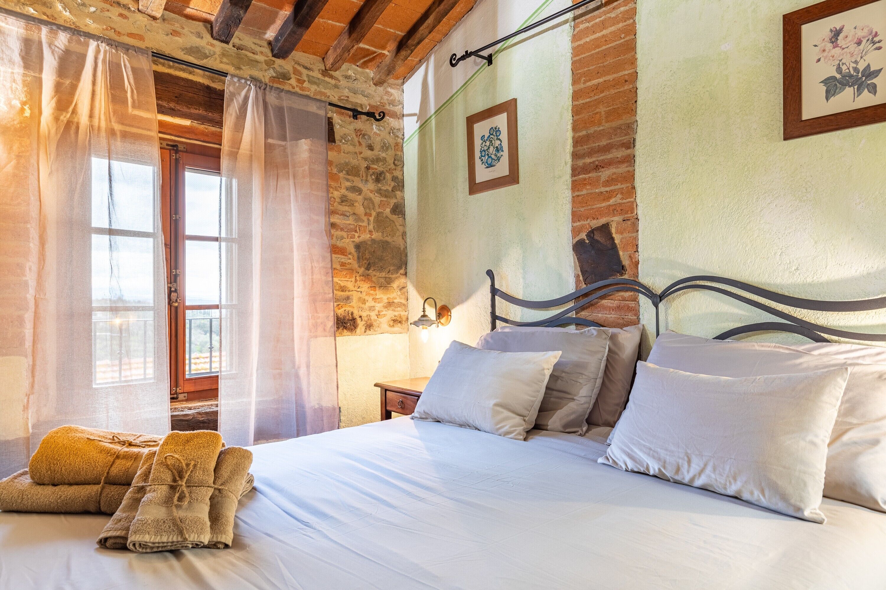 A bedroom with a bed, pillows, a nightstand, a lamp, and a window with curtains.
