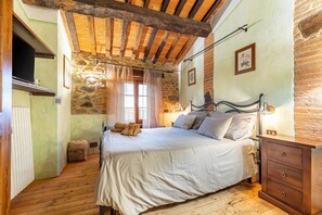 Un dormitorio con techo de madera, cama con ropa blanca, mesita de noche y pared de piedra.