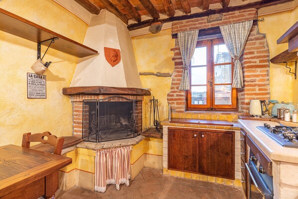 Una cocina rústica con pared de ladrillo, una mesa de madera, una estufa y una ventana con cortinas.