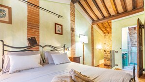 Un dormitorio con cama, almohadas, una mesita de noche con lámpara, una pared de ladrillo y techo de madera.