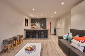 Een moderne keuken met een centraal eiland, barkrukken en een eettafel met fruit.