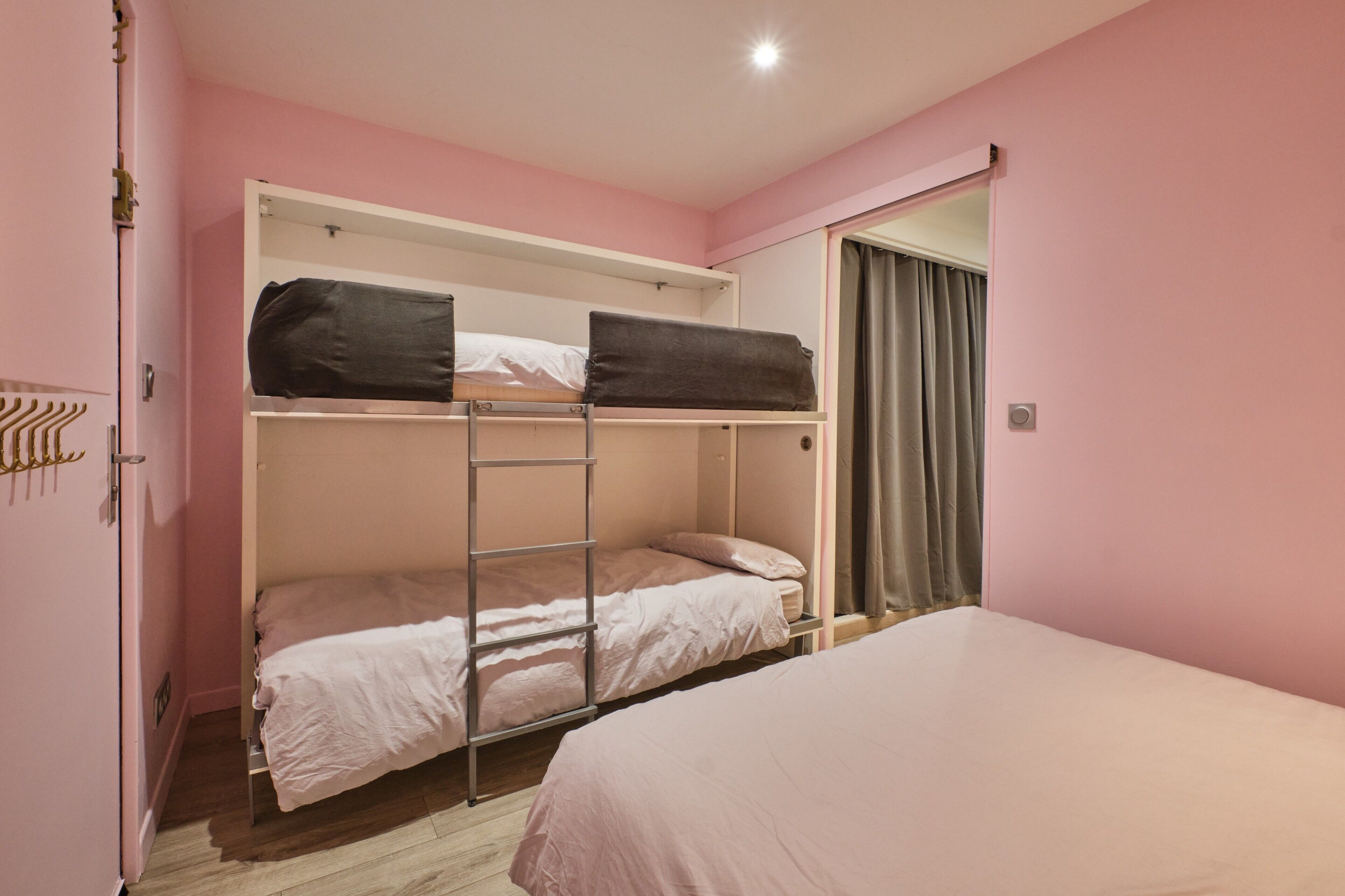 Une chambre avec un lit superposé, une échelle, une porte avec un porte-manteau et une fenêtre avec des rideaux.