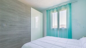 Ein Schlafzimmer mit Bett, einem Fenster mit Vorhängen und einer Wand mit Holzstruktur.