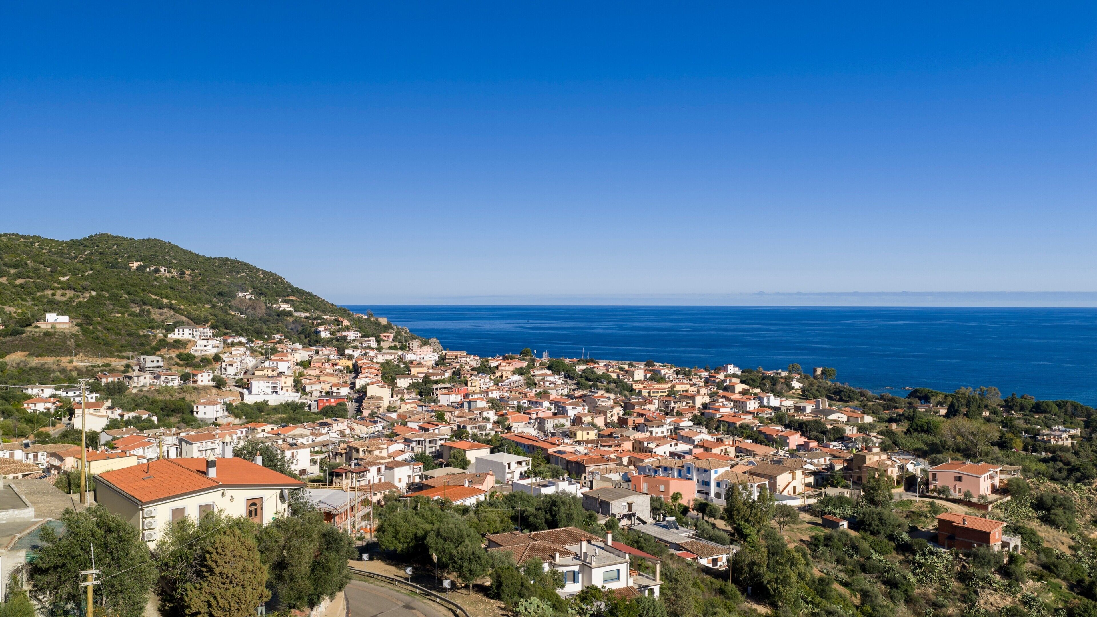 Un pueblo costero con un conjunto denso de edificios, un cielo azul claro y vistas al mar.