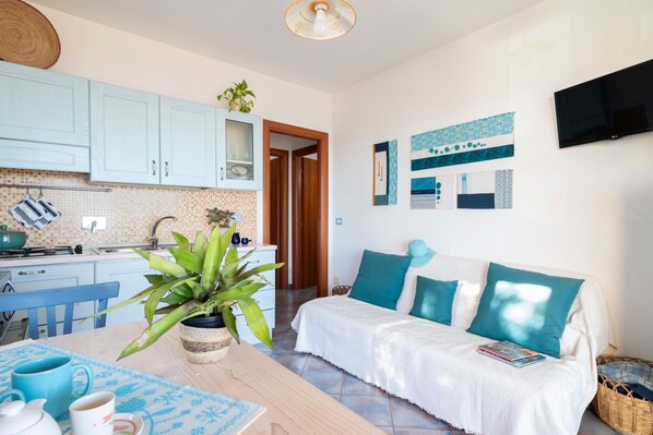 A modern kitchen with light blue cabinets, a dining table with blue placemats, and a cozy living area with a white sofa and teal cushions.