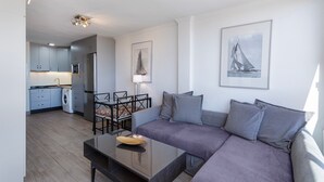 A modern living room with a sofa, a dining table, and a kitchen in the background.