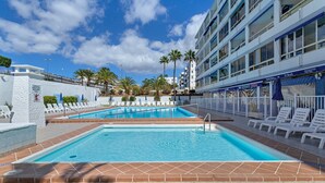 A swimming pool with lounge chairs, palm trees, and a building with balconies.