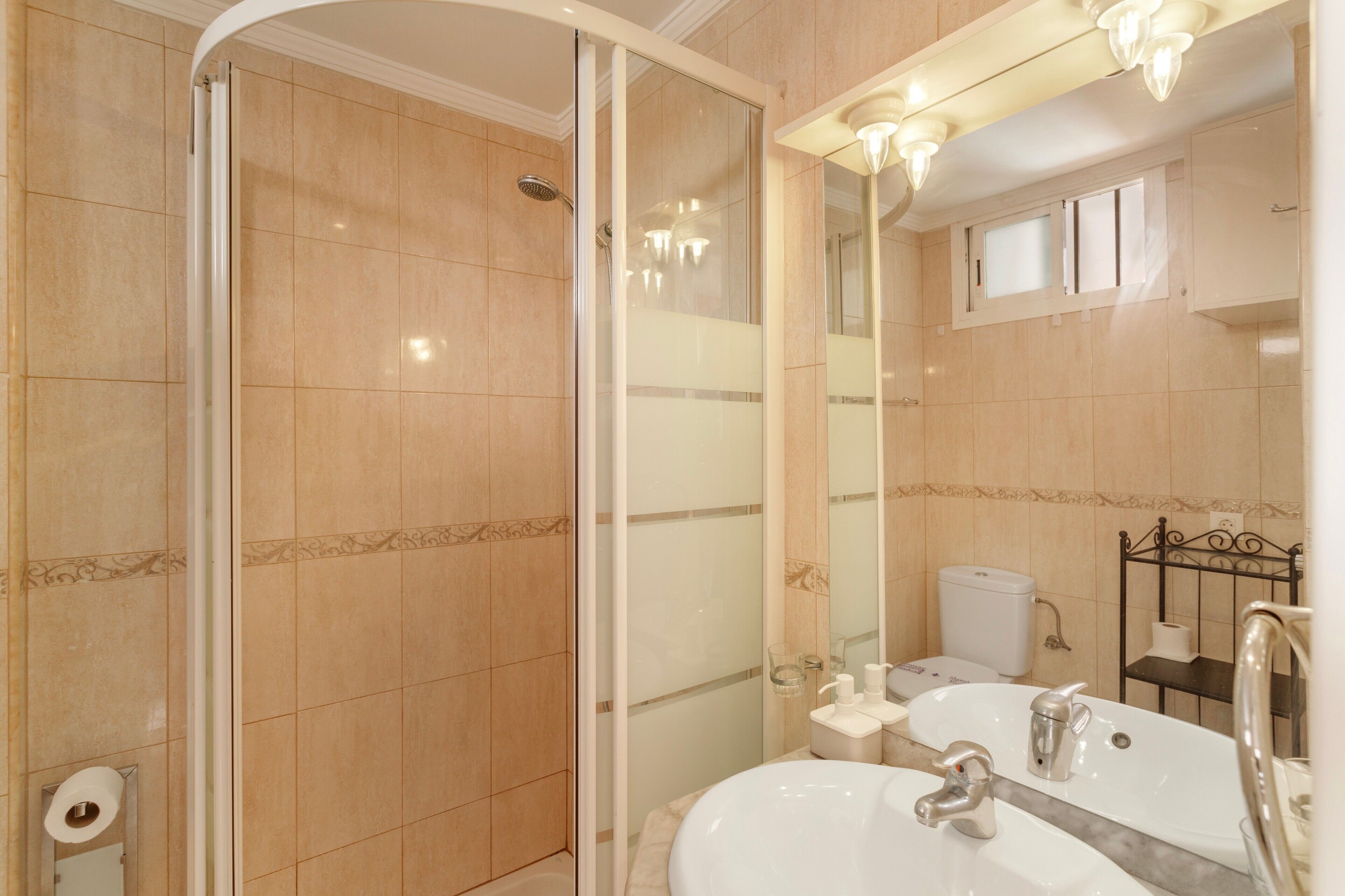 Un baño con ducha acristalada, lavamanos con espejo y retrete.