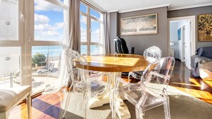A dining area with a wooden table and clear chairs, large windows with curtains, a painting on the wall, and a view of the sea. - Apartment 'Altea Beach' with Sea View, Wi-Fi and Air Conditioning (Altea)