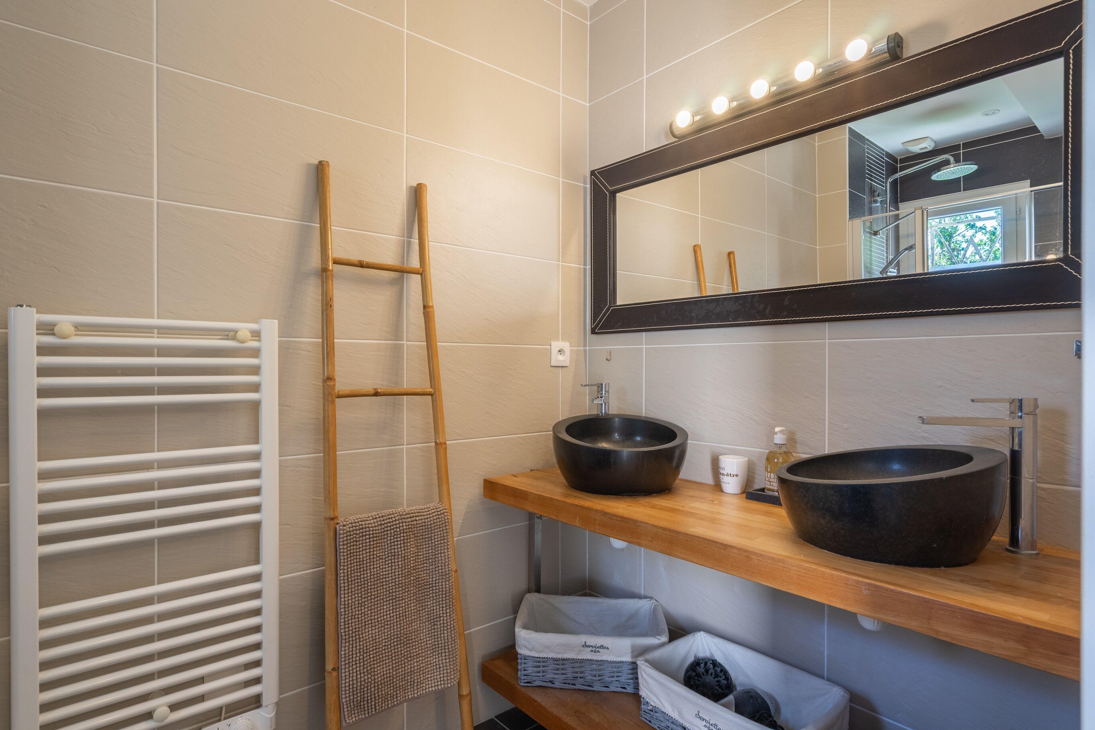 A bathroom with a wooden shelf, a large mirror, a towel rack, and a white radiator.