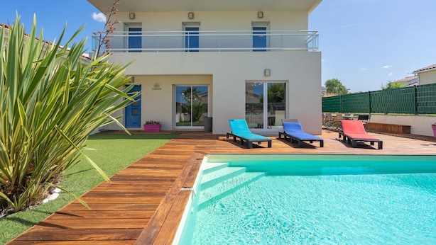 Une maison à deux étages avec une piscine, un balcon et un jardin agrémenté d’un palmier.