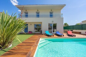 Ein zweistöckiges Haus mit Swimmingpool, Balkon und Garten mit einer Palme.