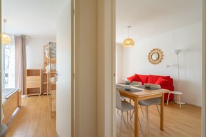Een moderne kamer met houten vloer, een eettafel met stoelen, een rode bank en een lamp.