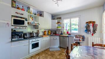 Una cocina con armarios blancos, microondas, cafetera y comedor con mesa y sillas.