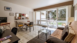 A living room with a sofa, coffee table, TV, and dining area with chairs and a table. - At Aux Pins Maritimes, with Beautiful Terrace - A22 (Pornic)