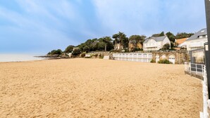 A sandy beach with a stone pier and buildings in the background. - At Aux Pins Maritimes, with Beautiful Terrace - A22 (Pornic)