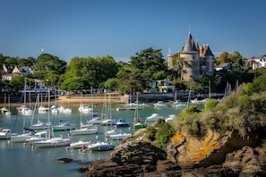 Une ville côtière dotée d’une tour historique, d’un port de plaisance avec des bateaux et d’une végétation luxuriante.