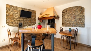 Un comedor con paredes de piedra, chimenea, televisor montado en la pared y una mesa con sillas.